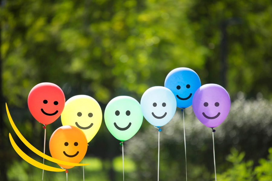 Colourful balloons with smiley faces in a row against a green outdoor background.