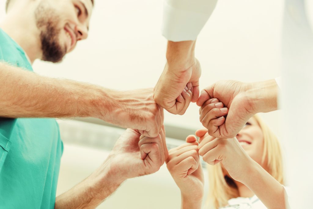 Group of people doing a team fist bump in a circle, viewed from below.